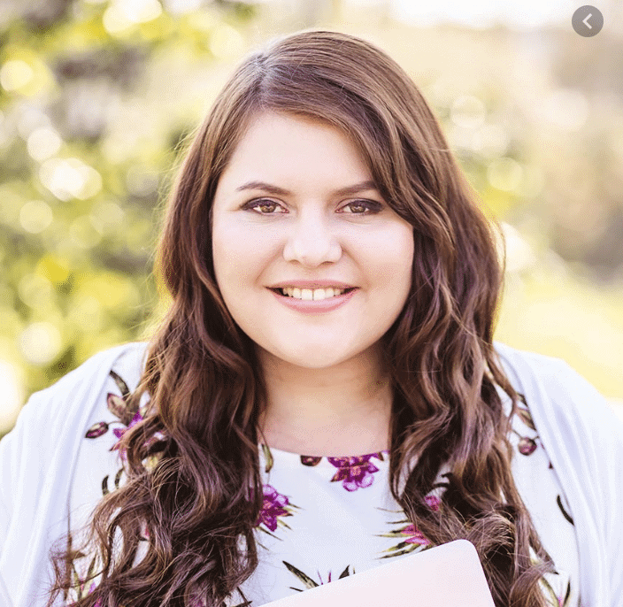 A woman with long hair and a white cardigan smiles for the camera